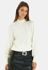 Witte gebreide trui met een hoge kraag, voorzien van geplooide lange mouwen en een geplooide halslijn. Gecombineerd met een zwarte leren rok en een versierde riem.