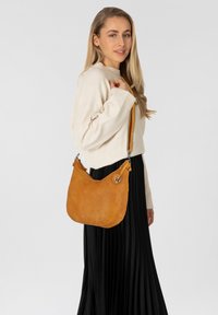 Borsa a spalla in pelle gialla con una forma curva distintiva, dotata di un charm ancorato decorativo e di una tracolla corta e regolabile.