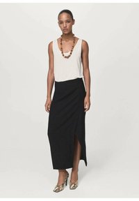 Falda negra hasta los tobillos con una abertura frontal, combinada con una blusa blanca sin mangas de corte holgado. Collar de cuentas en tonos cálidos. Tacones con estampado de serpiente.