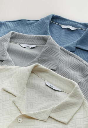 Tre polo-shirts i lys blå, lysegrå og creme. Hver har et tekstureret mønster og en klassisk krave. Mærket er synligt.