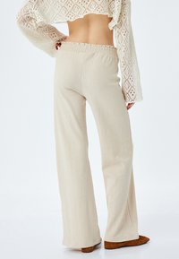 Beige, textuurrijke broek met wijde pijpen en een elastische tailleband. De stof heeft een subtiel geribbeld patroon dat doorloopt tot aan de enkels.
