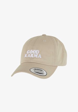 Vaaleanbeige puuvillalippis, jossa on säädettävä hihna, edessä valkoisella brodeerattu teksti "GOOD KARMA" ja suora, muotoiltu lippa.