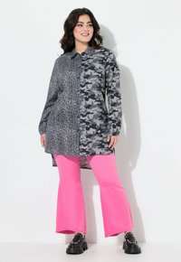 Skjorte med knaplukning og split-design: den ene side er leopardprint, den anden er camouflage; parret med lyserøde flagrende bukser og sorte platform sko.