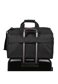 Schwarze Stoff-Reisetasche mit doppelt genähten Griffen, Reißverschluss und einem Rückengurt zum Anbringen an Gepäckgriffen. Glatte Oberfläche, minimales Design.
