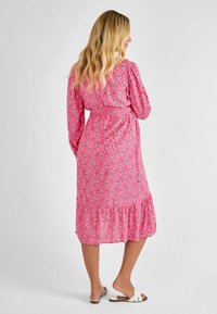 Robe enveloppante à motifs rose avec des manches longues, dotée d'un ourlet volanté et d'une ceinture à nouer. Le tissu a une texture douce avec des motifs géométriques.