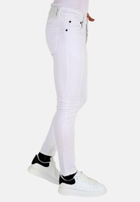 Witte skinny jeans van denim, met een middelhoge taille, vijf zakken en zwarte accenten op de knoop en klinknagels. Draag ze met witte sneakers.