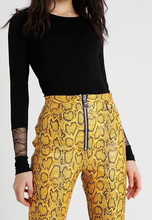 Un haut noir à manches longues avec des accents en dentelle, associé à un pantalon taille haute en imprimé serpent jaune avec une fermeture éclair devant et une finition texturée.