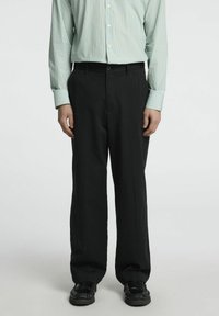 Juodos kelnės tiesaus kirpimo, derinamos su žaliai dryžuota ilgomis rankovėmis marškiniais. Atrodo, kad medžiaga yra audinė, su lygiu paviršiumi.