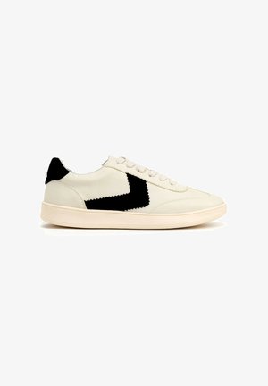 Baskets en cuir blanc avec un accent zigzag noir, bout rond et conception à lacets. Présente une texture lisse et une semelle en caoutchouc à profil bas.
