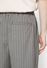 Szare spodnie w paski o dopasowanym kroju, charakteryzujące się gładką fakturą, dwoma tylkimi kieszeniami oraz pasem. Akcentowane cienkimi pionowymi białymi paskami.