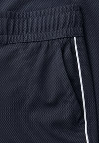 Tela azul marino con pequeños puntos blancos, cintura elástica, bolsillo lateral y detalle de ribete blanco en un par de pantalones o pantalones cortos.