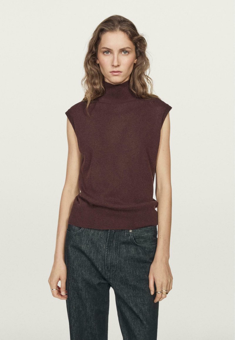 Top senza maniche bordeaux con collo alto realizzato in morbido tessuto a maglia, abbinato a jeans in denim scuro. Design minimalista con una silhouette aderente.