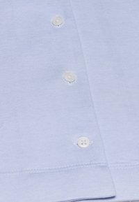 Hellblaues T-Shirt mit kurzen Ärmeln und glatter Textur, mit drei weißen Knöpfen in einer Reihe und einem geraden Saum am unteren Ende.