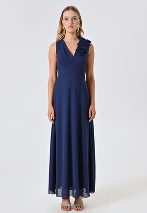 Marineblaues ärmelloses Kleid mit V-Ausschnitt, gerafftem Oberteil und floralem Akzent an einer Schulter. Fließender Rock mit leichtem Glanz.