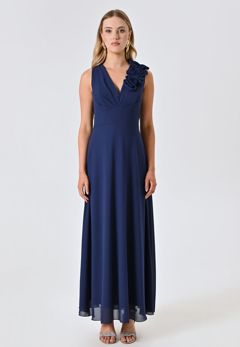 Marineblaues ärmelloses Kleid mit V-Ausschnitt, gerafftem Oberteil und floralem Akzent an einer Schulter. Fließender Rock mit leichtem Glanz.