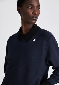 Felpa navy con colletto nero, tessuto testurizzato e un piccolo logo argento sul colletto. Presenta un collo a giro e una vestibilità comoda.
