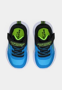 Dětské modré tenisky Skechers S-Lights s černými popruhy, neonově zelenými stélkami a bílou podrážkou, zobrazené shora na bílém pozadí.