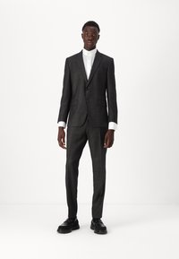 Mørkegrå jakkesæt med en slim fit, der har en enkeltknap blazer og lige bukser. Komplementeret af en hvid skjorte med krave og sorte sko.