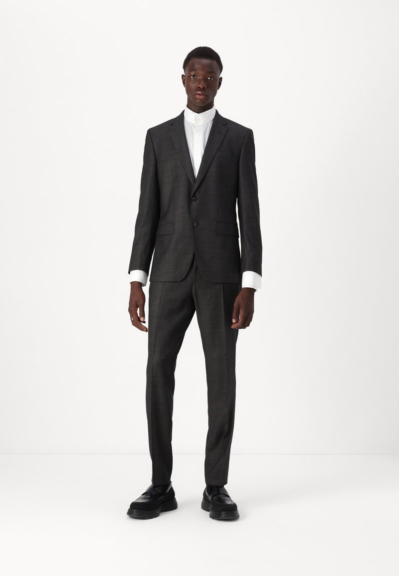 Mørkegrå jakkesæt med en slim fit, der har en enkeltknap blazer og lige bukser. Komplementeret af en hvid skjorte med krave og sorte sko.