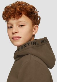 Hoodie marrone scuro con un grande cappuccio morbido e testo nero lungo il colletto. Tessuto liscio con dettagli di cucitura visibili.