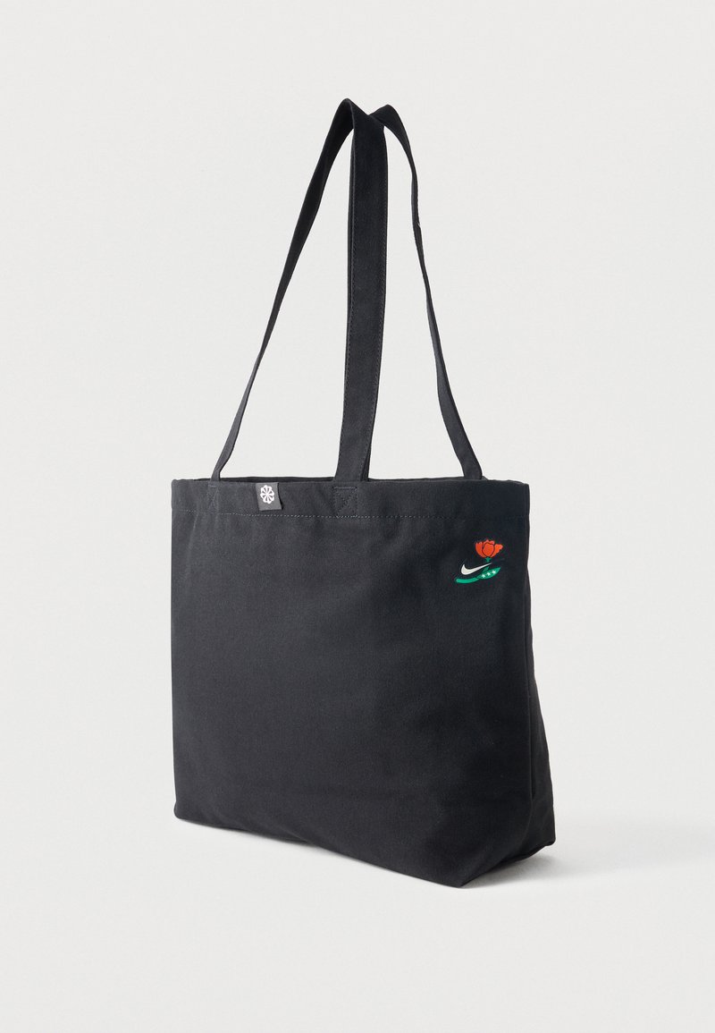 Bolso tote negro con asas largas, con una pequeña rosa roja y el logo blanco de Nike swoosh en la esquina superior derecha.