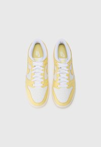 Sneaker gialle e bianche con punta perforata, parte superiore in pelle liscia, dettagli in contrasto e lacci bianchi. Suola in gomma piatta.