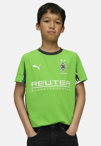 Zielona koszulka z krótkim rękawem z czarnymi akcentami, z logo i białym napisem. Rękawy boczne mają wzór w kamuflażu. Wykonana z oddychającego materiału.