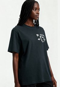 T-shirt en coton noir à manches courtes, col rond, avec un design graphique en texte blanc et une flèche sur la poitrine. Texture lisse.