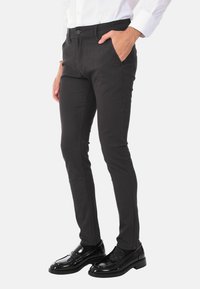 Pantaloni neri slim-fit in tessuto texture, con tasche frontali e chiusura con bottone, abbinati a mocassini neri lucidi.