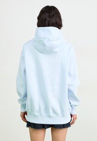 Sweatshirt azul claro com capuz, de corte descontraído, punhos e bainha canelados, e uma textura suave. A parte de trás possui um bolso canguru.
