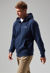 Navy blue zip-up hoodie with a drawstring hood, soft texture, front pockets, and a small white logo on the chest.
