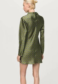 Vestido verde con patrón, de textura suave, que presenta mangas largas y un cuello, mostrando un diseño geométrico en azul oscuro y verde claro.
