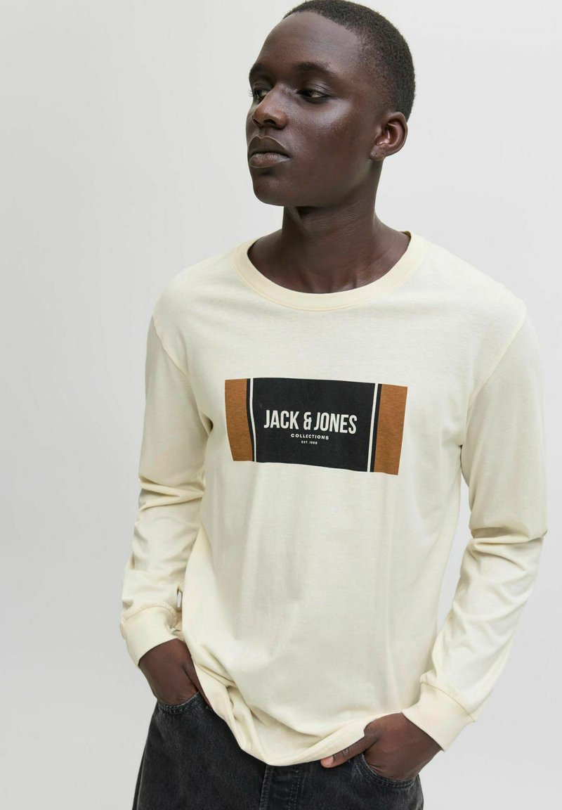 Kreemjast pikast varrukast t-särk, mille esiküljel on musta ja pruunika ristkülikukujuline logo, millel on kiri "JACK & JONES COLLECTIONS".