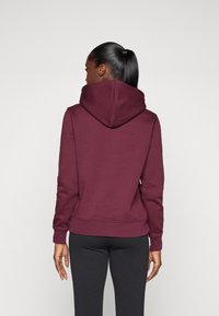 Sweatshirt à capuche bordeaux avec une coupe décontractée, des poignets côtelés et une poche kangourou. Texture de tissu lisse et coutures double piqûre.
