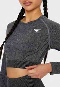 Sivi dugi crop top s dugim rukavima, izrađen od teksturirane tkanine, s kontrastnim šavovima i logotipom na prsima. Uski kroj s rebrastim rubom.