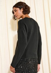 Melnas adītas džemperis ar ribotu apakšmalu un piedurknēm, ar apaļu kakla izgriezumu un smalku tekstūru, kombinēts ar melnu fliteru svārku.