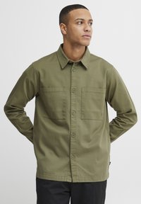 Olive green button-up shirt made of smooth fabric, featuring two chest pockets and a collared neckline, with long sleeves and straight hem.