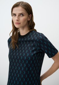 Top a maniche corte con un motivo geometrico in blu e nero. Realizzato in un tessuto testurizzato con un collo a contrasto nero.