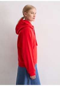 Rode hoodie met een ontspannen pasvorm, koorddetail en geribde mouwen, gecombineerd met een blauwe denim rok. Gladde textuur.