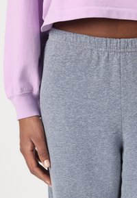 Vaalean violetti lyhyt huppari, jossa on ribbaus hihansuissa, viereen on aseteltu harmaat heather-sweatpantsit, joissa on joustava vyötärö ja sileä pinta.