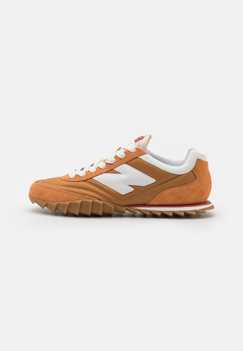 Orange mockasinsneakers med vita accenter, texturerad yttersula och snörning med sex ögon. Har en logotyp på sidan och röda detaljer.