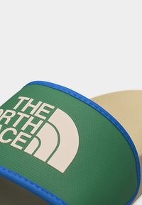 Πράσινος και μπλε λουρί σαμπό με μεγάλο λευκό λογότυπο και κείμενο The North Face στο κέντρο του λουριού.