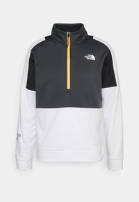 Sudadera de media cremallera en gris oscuro, blanco y negro. Tejido texturizado con cremallera amarilla. Cuenta con el logo en el pecho y en la manga.