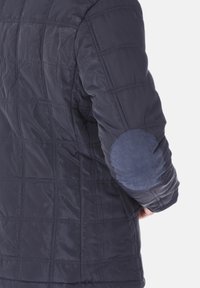 Giubbotto trapuntato blu navy con una finitura testurizzata, caratterizzato da un toppa blu a contrasto sui gomiti e un design a taglio dritto.