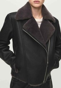 Czarna skórzana kurtka z szarym futrzanym kołnierzem, przednim suwakiem i bocznymi kieszeniami, o skróconym kroju i miękkiej fakturze.