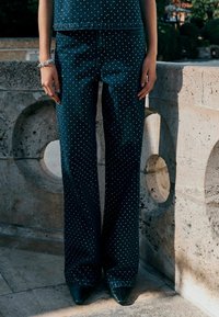 Platus džinsinis kelnes su baltais taškeliais, tamsiai mėlynos spalvos audinys ir lygi tekstūra. Suderinta su juodais batais su smailiu nosimi.