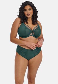Groene lingerie set bestaande uit een gestructureerde beha met netpanelen en een ingewikkeld uitsnijdontwerp, gecombineerd met hoge slips.