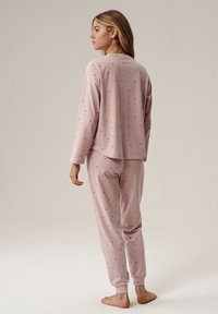 Różowe piżamy z długim rękawem w formie koszulki z okrągłym dekoltem oraz zwężającymi się spodniami w małe czarne kropki. Miękki materiał i luźny krój.