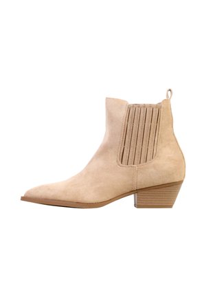 Bottine beige en daim avec bout pointu, panneaux latéraux élastiques, languette au talon et petit talon bloc empilé.