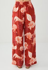 Rode bloemenprint losse broek met een elastische tailleband, voorzien van witte bloemen en bladeren, gemaakt van lichtgewicht stof met een zachte textuur.